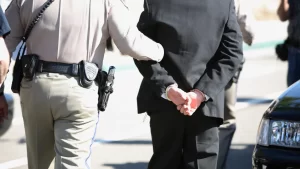 a police officer walking a cuffed drunk man to the police vehicle