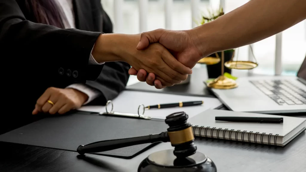 Client and juvenile criminal defense lawyer in Cincinnati shaking hands over a desk decorated with gavel and scales of justice.