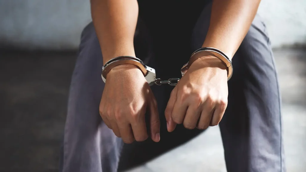 A person sitting with hands cuffed in front.
