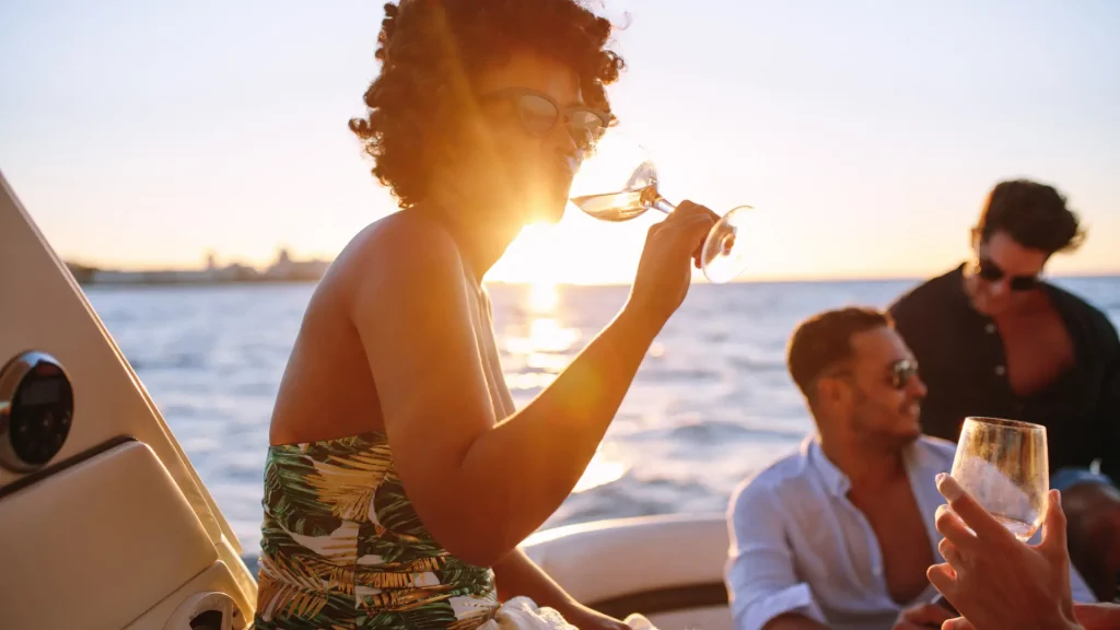 A woman enjoying a drink on a boat while watching the sunset, with a man in the background.